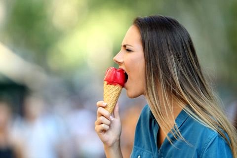 Woman painfully contorts face while eating ice cream.