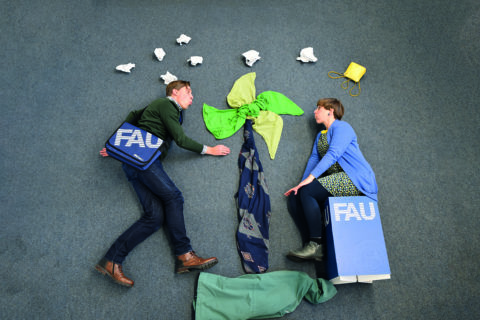 two people on the floor in stopmotion style next to a windmill made of clothes