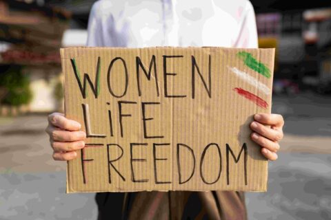 A woman holds a sign in her hands. It reads "Women Life Freedom.