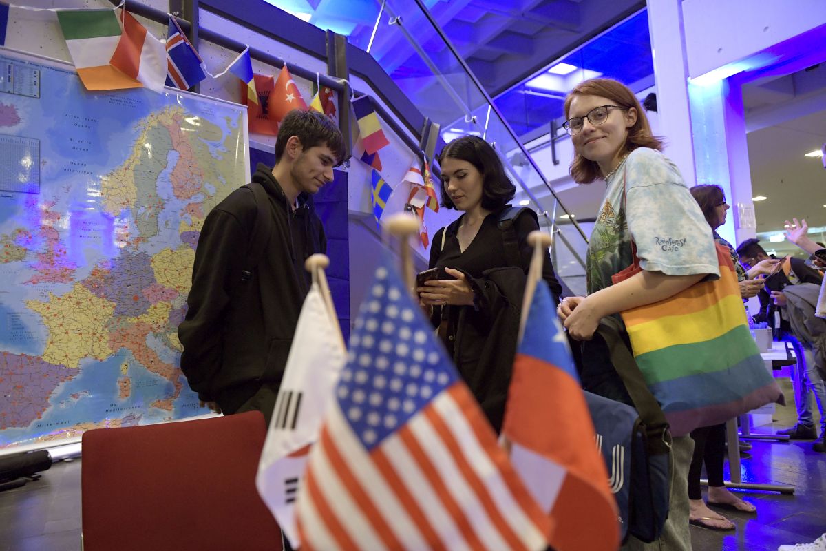 Photo of a young man and two young women surrounded by several national flags