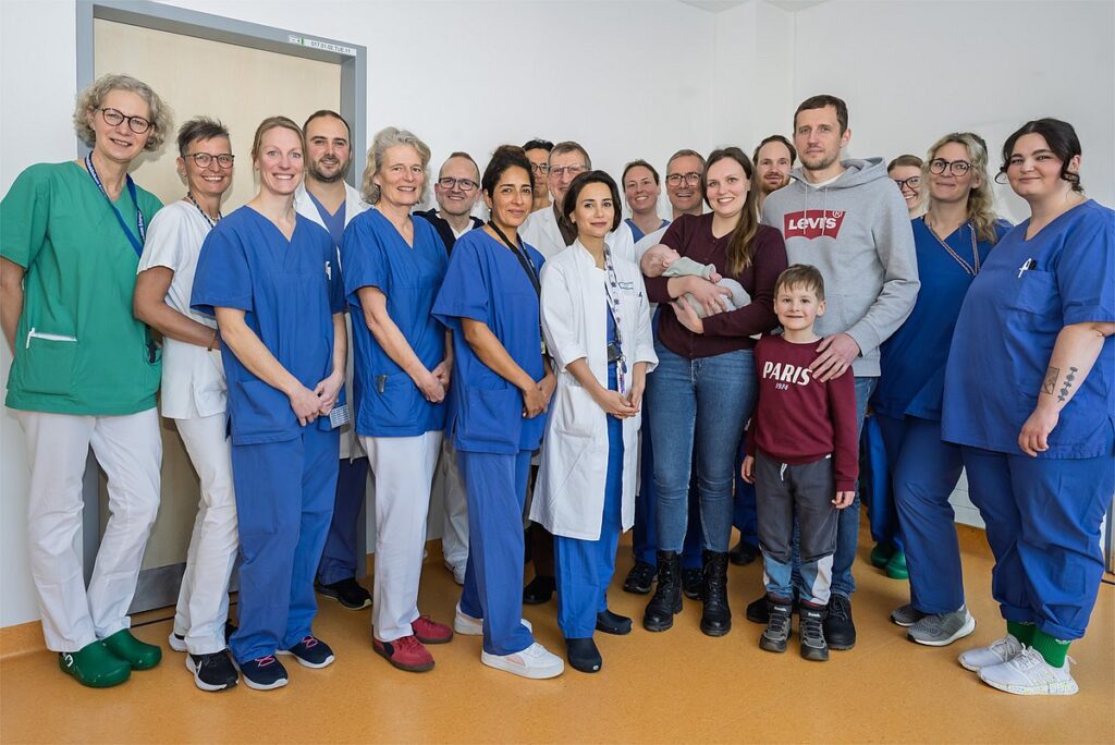 Teamwork: 16 doctors and nurses from the Department of Pediatrics and Adolescent Medicine at Uniklinikum Erlangen gather around the parents of little David, his twin sister Adele and his big brother Lev. David is still lying in his crib in neonatology at this time. Image: Michael Rabenstein/Uniklinikum Erlangen