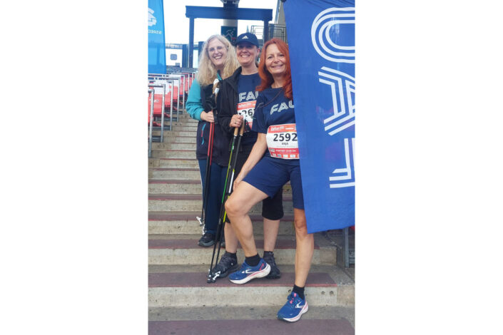 Drei Mitglieder des FAU-Teams auf einer Treppe im Stadion mit FAU-Flagge