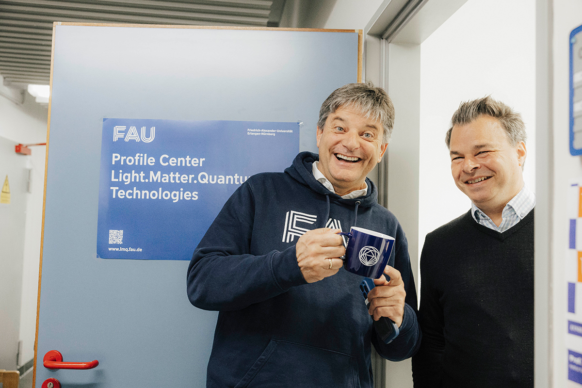 Kai Phillip Schmidt and Joachim Hornegger pose together. Hornegger is smiling and holding an FAU mug.