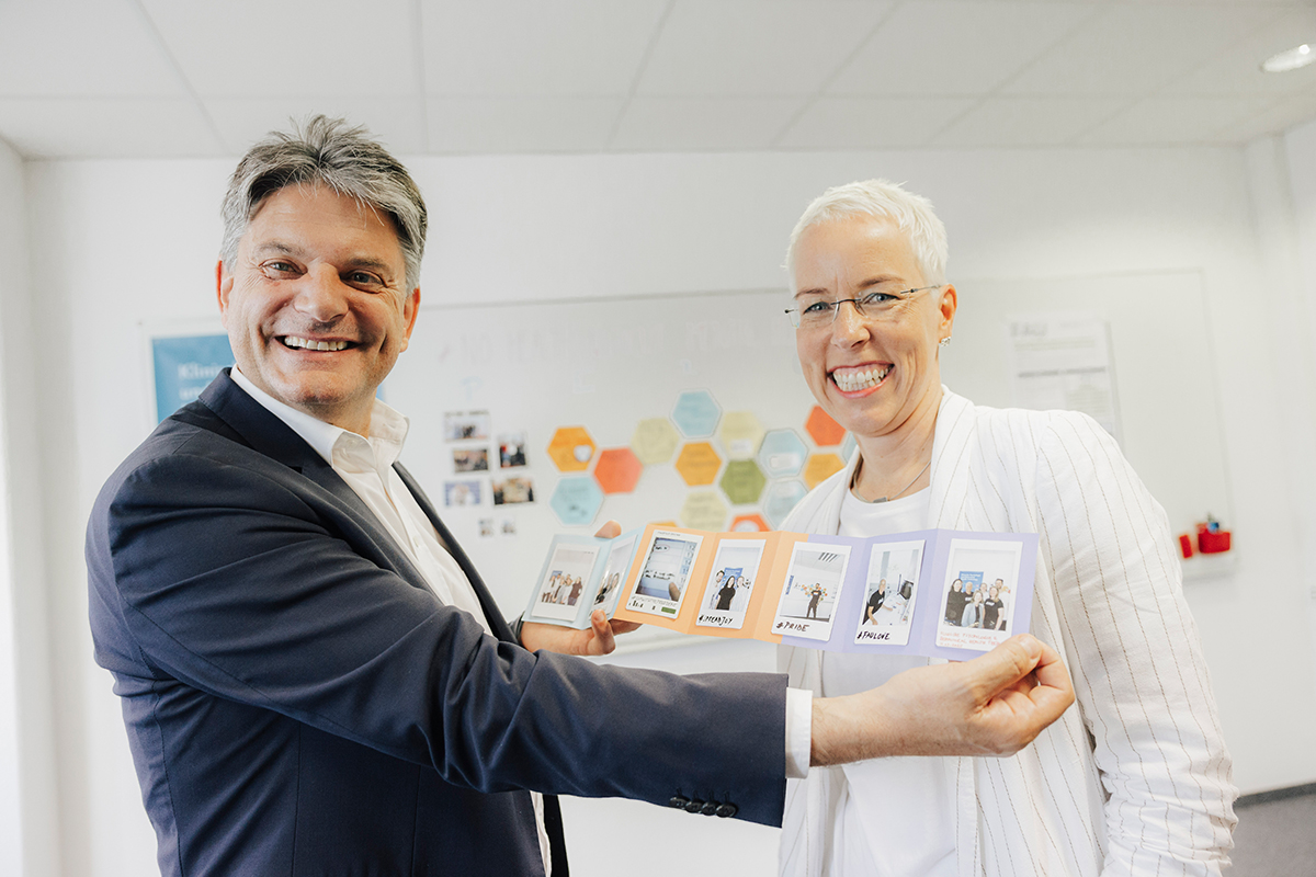 President Hornegger and Prof. Weise are standing smiling next to each other posing for a photo. President Hornegger is showing a series of Polaroid photos.