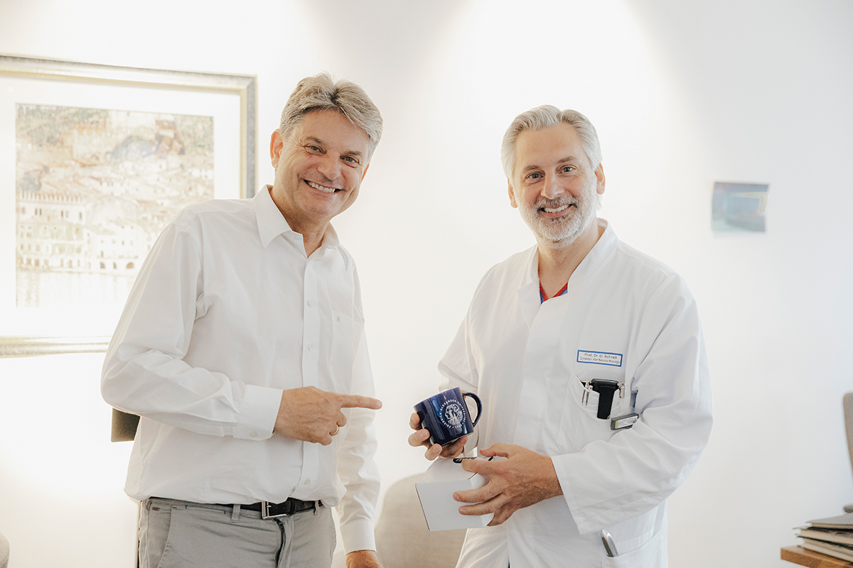 Prof. Schnell and President Hornegger are standing next to each other and smiling into the camera. Oliver Schnell is holding a cup, Hornegger is pointing towards it.