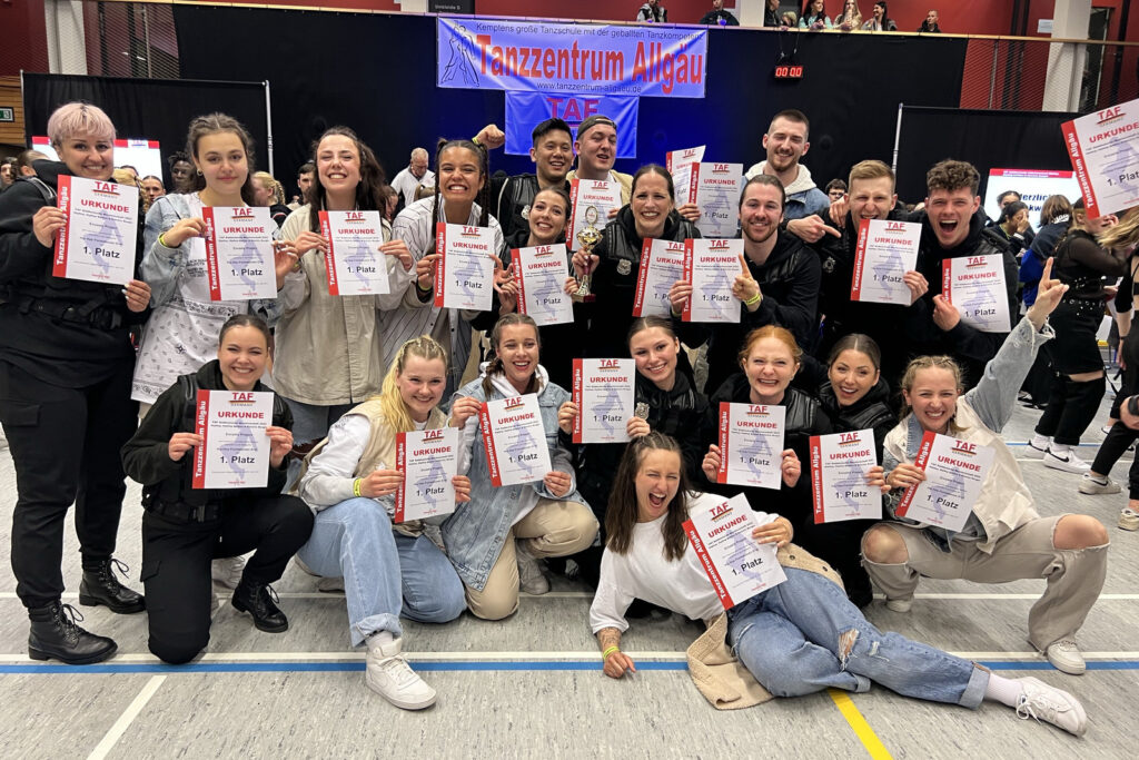 Approximately 20 people posing for a photo in a sports hall. They are all smiling and holding up certificates.