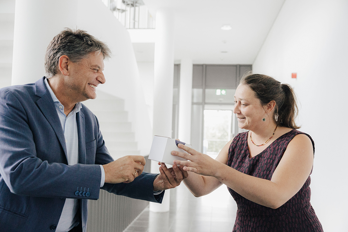 Prof. Hutter and Hornegger are standing in a light corridor, president Hornegger is handing a cup to Prof. Hutter.