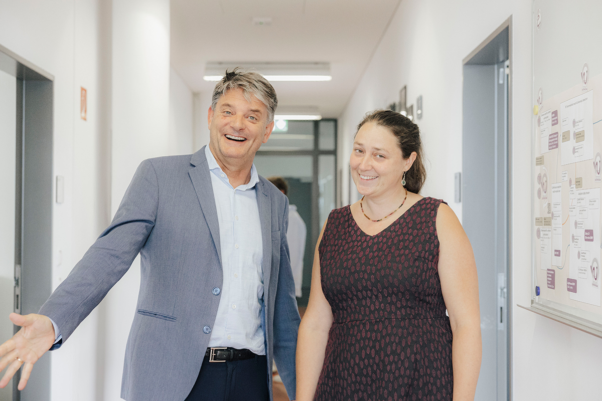 Prof. Jana Hutter and President Hornegger are standing together in a corridor. They are both smiling at the calendar, Hornegger is holding his left arm out to the side in an inviting gesture.