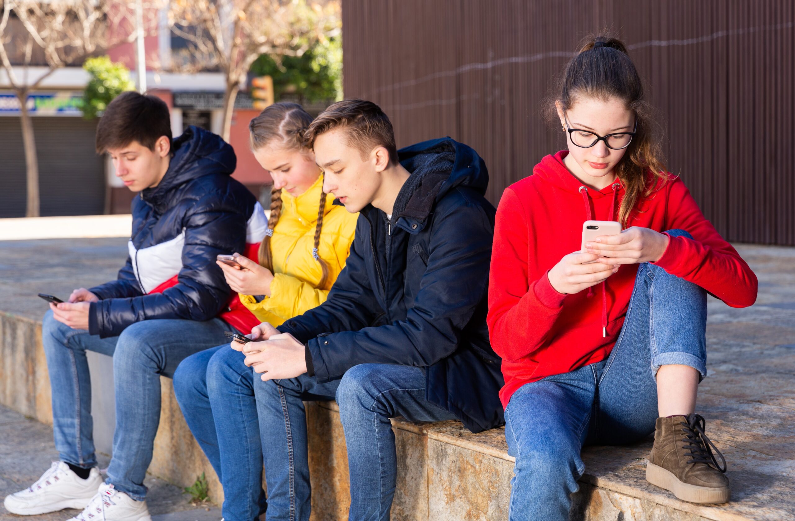 Vier Jugendliche, 2 Jungs, 2 Mädchen, sitzen beisammen und schauen auf ihre Smartphones.