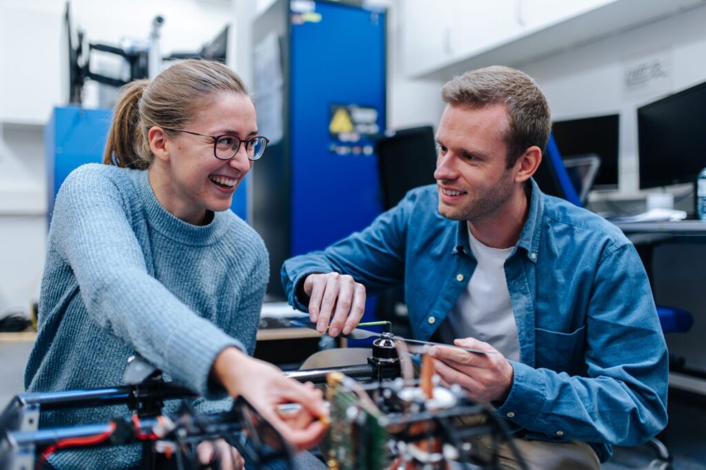 Eine junge Frau und ein junger Mann unterhalten sich angeregt, während sie etwas an einer technischen Einrichtung einstellen.