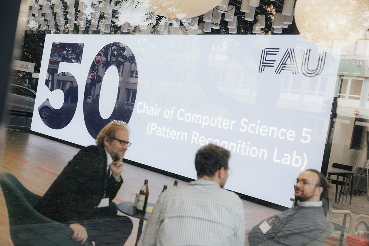 Eine Projektion mit 50 Years of Chair for Pattern Recognition. Im Vordergrund drei Männer die sich unterhalten.