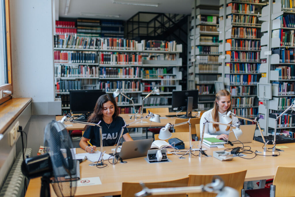 Two women sitting with laptops in a library.