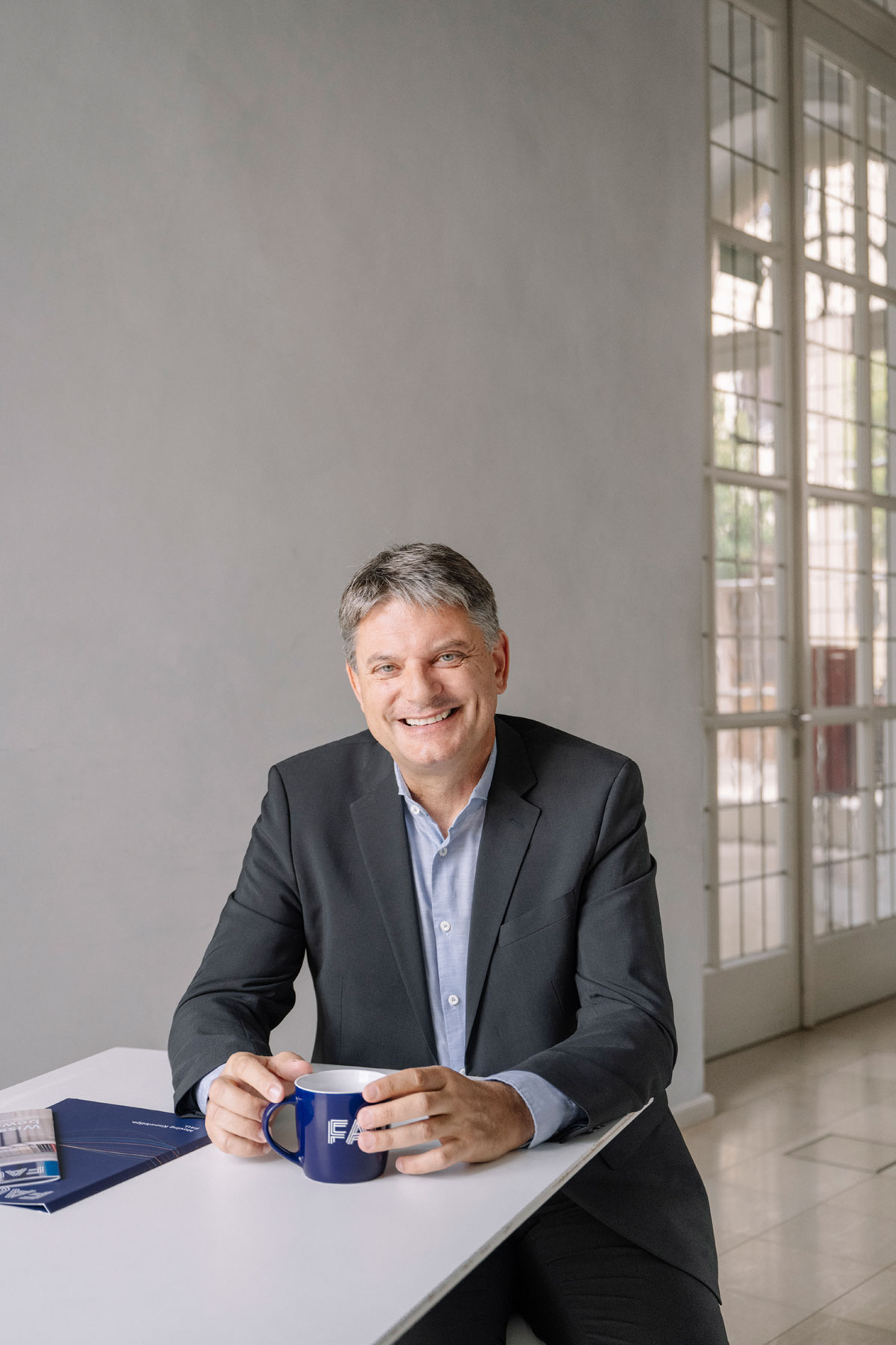 Joachim Hornegger sitzt mit Kaffeetasse an einem Tisch und lacht in die Kamera.
