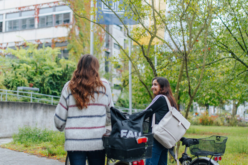 Zwei Studentinnen schieben ihr Fahrrad und schauen zurück.