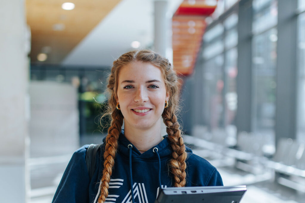Frau mit Laptop in der Hand schaut in die Kamera