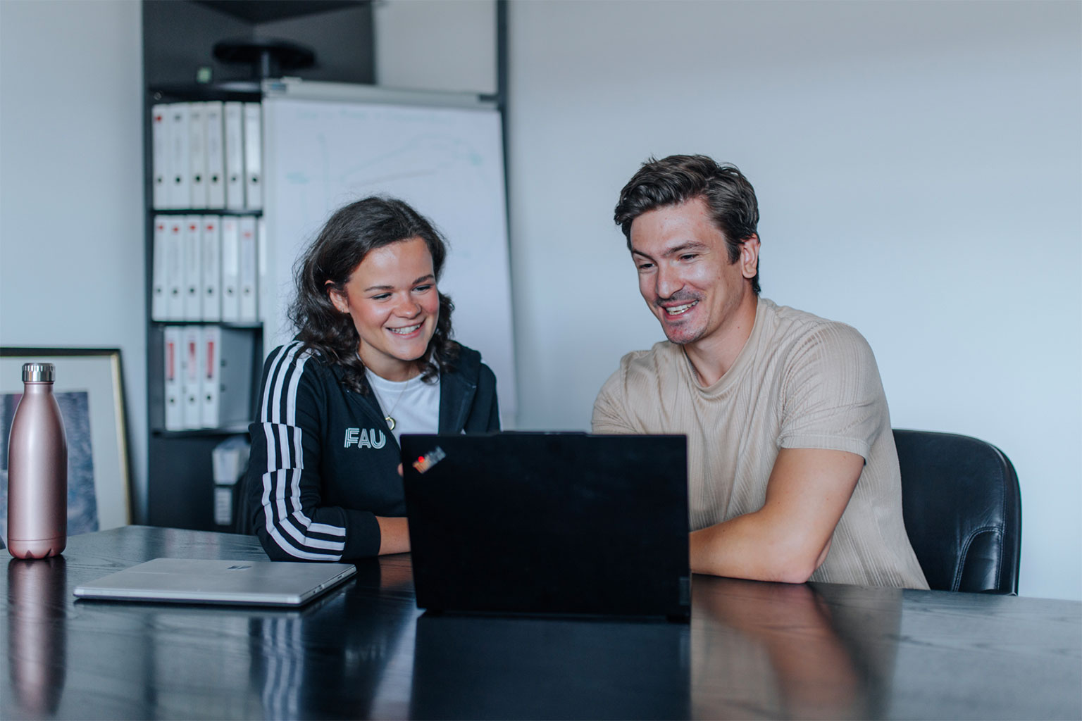 Eine junge Frau und ein junger Mann sitzen vor einem Laptop und besprechen sich.