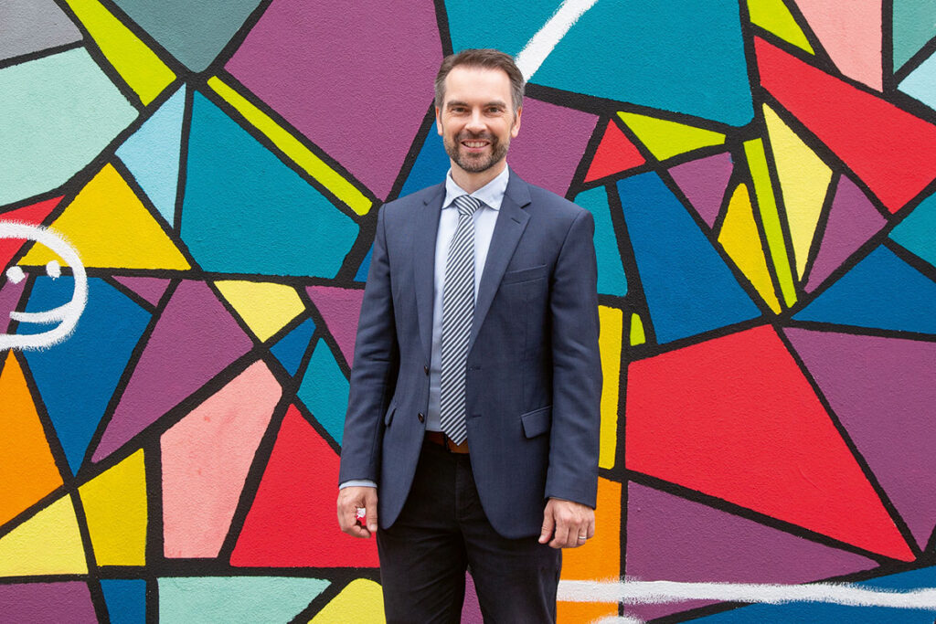 Prof. Dr. Andreas Ramming in front of a colorful wall.