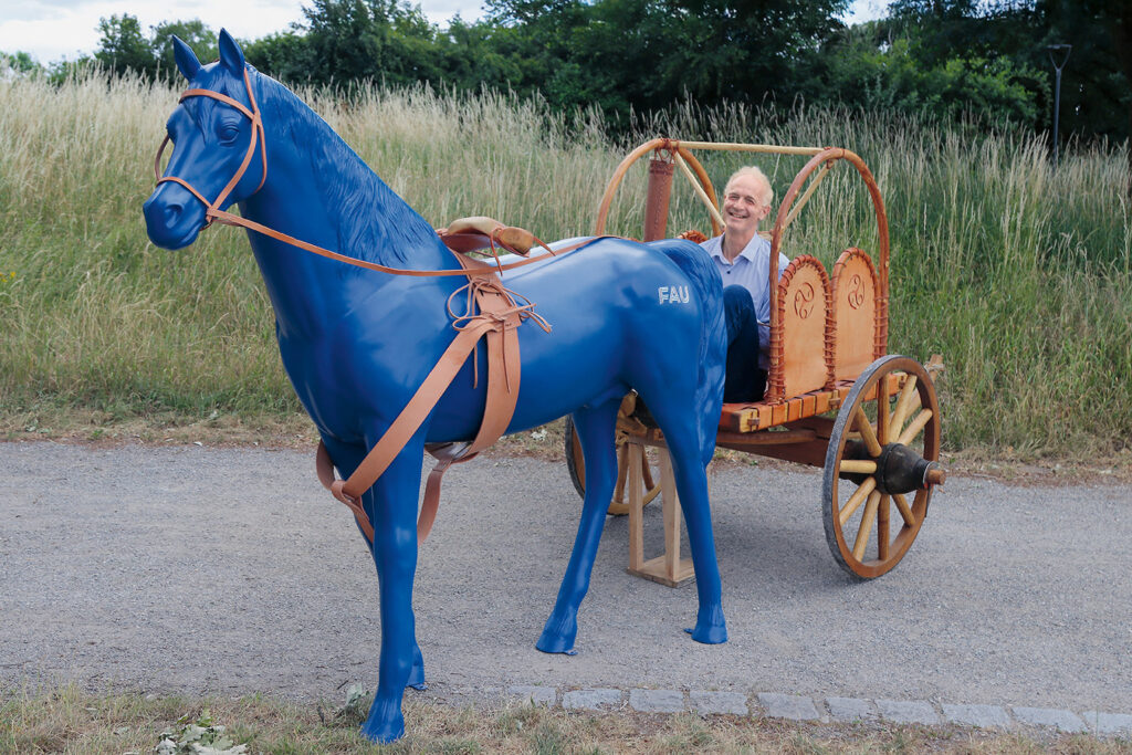 Boris Dreyer sits on a chariot. In front of him: A blue plastic horse.