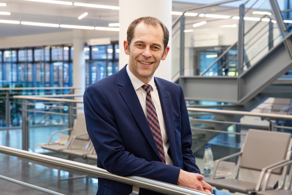 Professor Link is facing the camera and smiling. He wears a suit and stands in the foyer of a hospital.