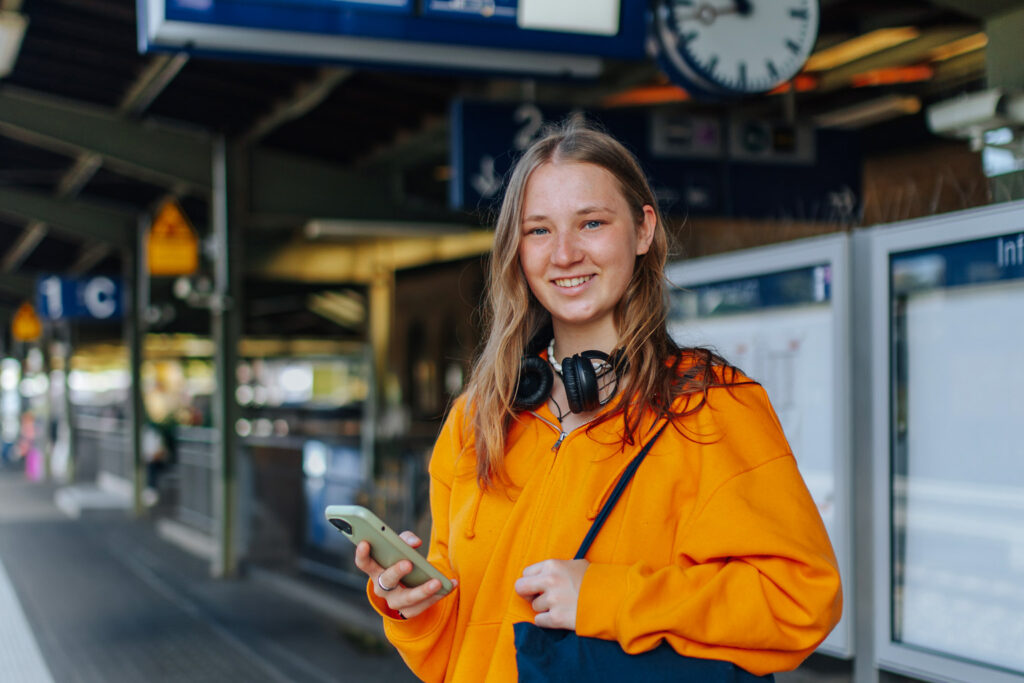 Studentin mit Handy am Bahnhof