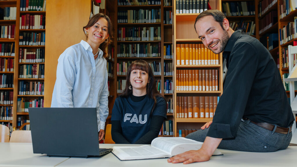 Three scientists in a library, sitting together in front of a laptop.