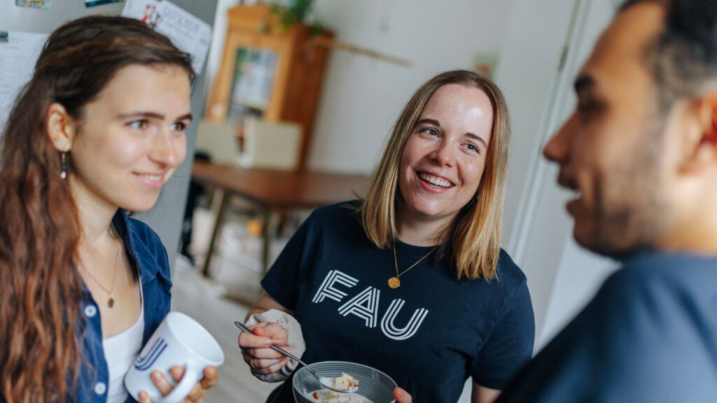 Three students with cups in a kitchen.