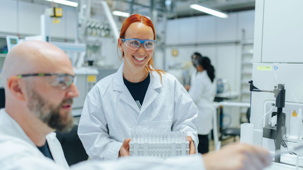 Two researchers in a lab. Both of them are waering glasses.