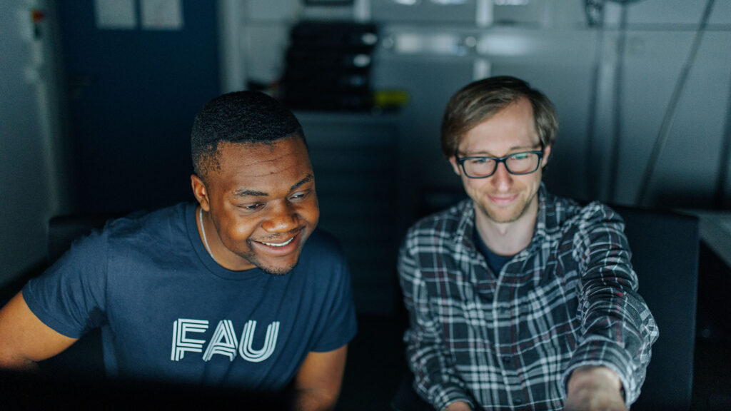 Two researchers in front of two screens in a dark room.