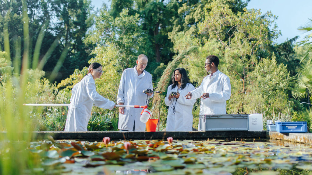 Four researchers with research tools are standing in front of a water basin.