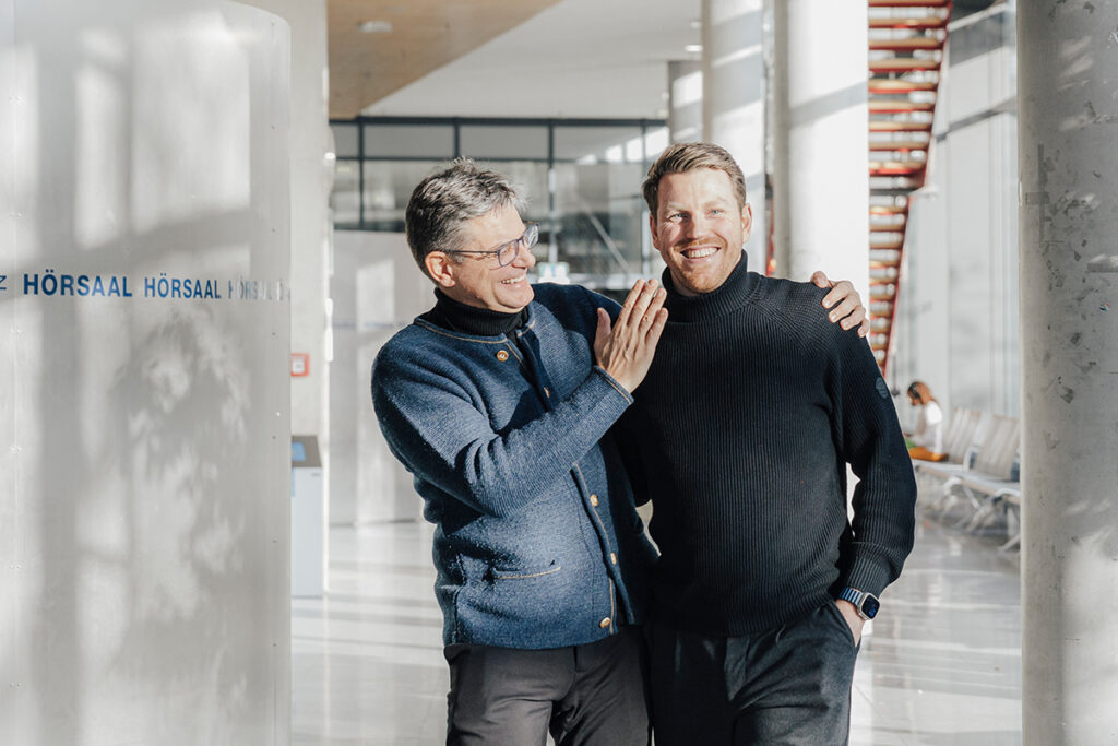 Joachim Hornegger and Marvin Nipper are walking arm in arm through a hallway.