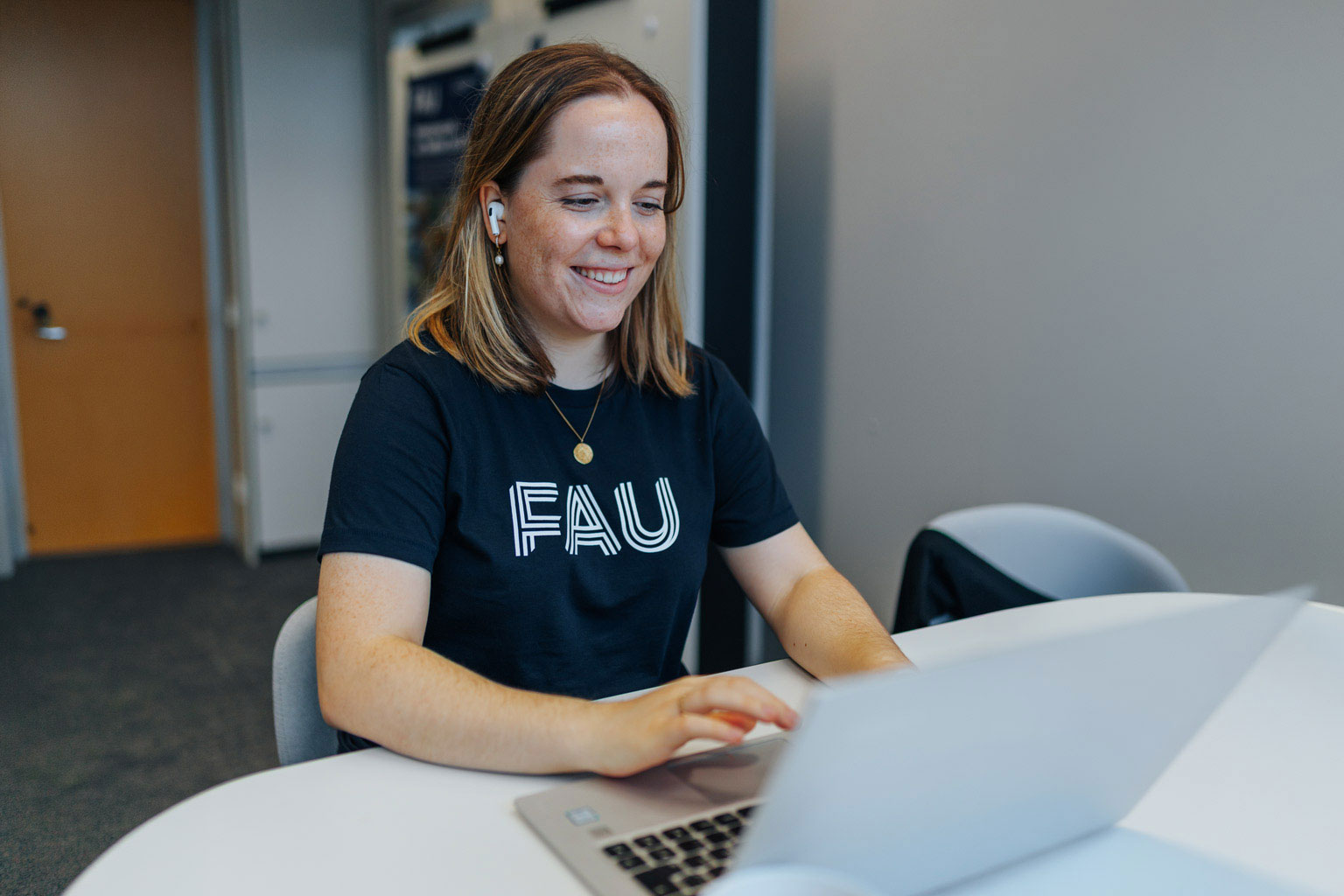 Studentin sitzt in einem Büro am Tisch und tippt in ihren Laptop.