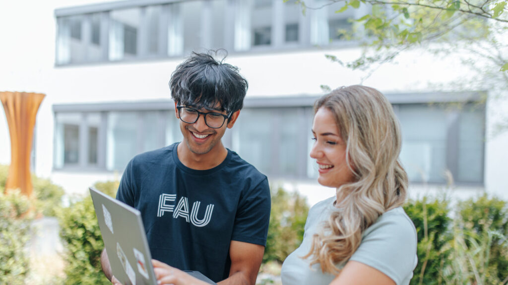 Two students standing together, looking in a laptop.