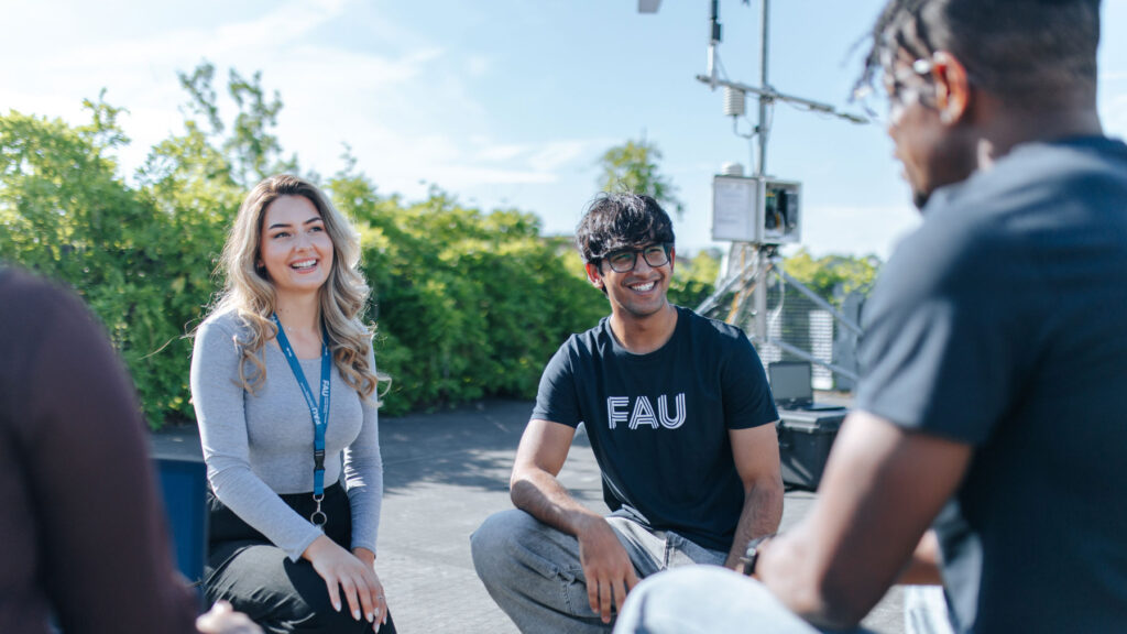 Four students sit together on the ground, talking to each other.