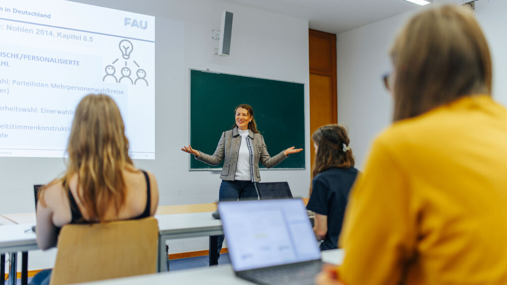 A lecturer is giving a presentation; three people are listening.