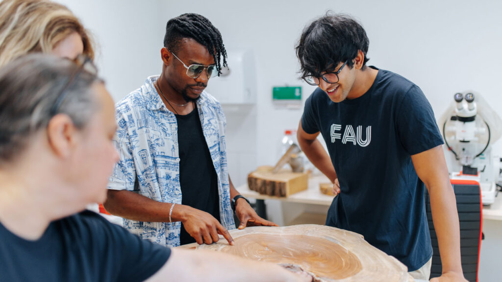 Students stand together and examine the growth rings of a tree trunk.