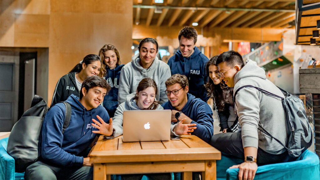 Nine students gather round a laptop.