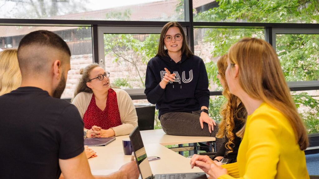 Several students are sitting together in a seminar room, discussing.