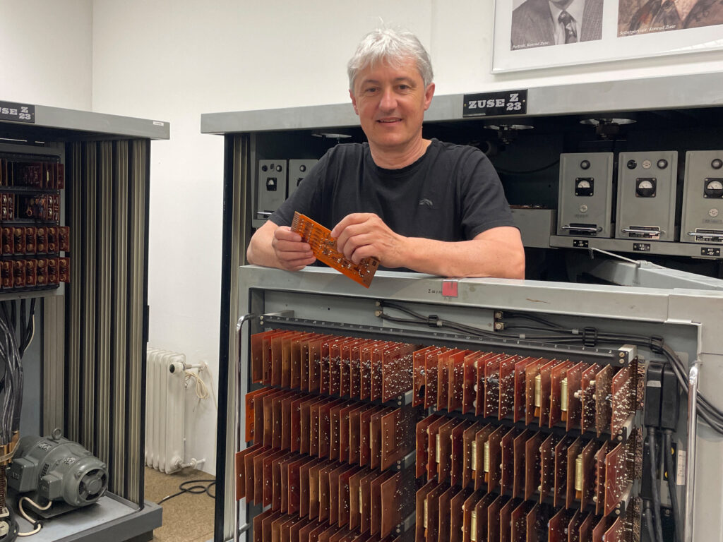 ein älterer Mann mit grauen Haaren hält eine alte Platine in der Hand.