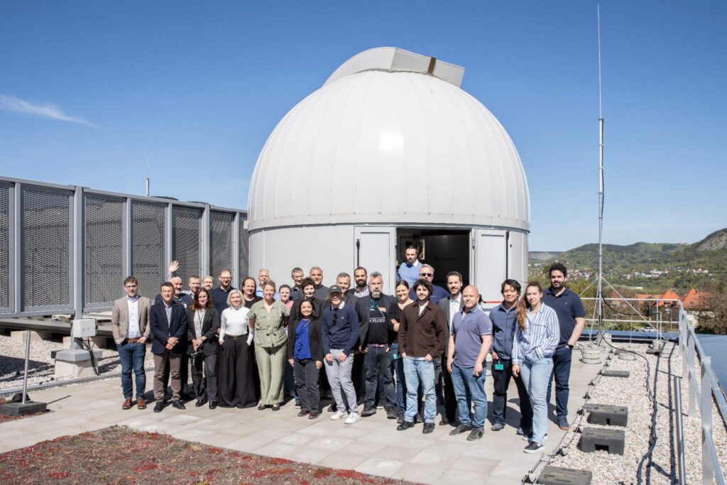 Group photo of the researchers in front of the dome of a telescope on a rooftop.