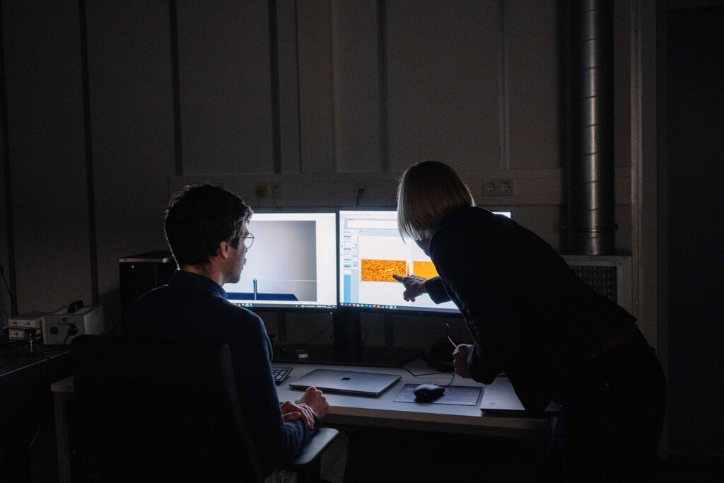 Two scientists in a dark room in front of a computer.