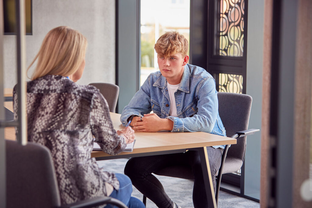 A young man and a woman are sitting at a table. The man is asking the woman for advice.