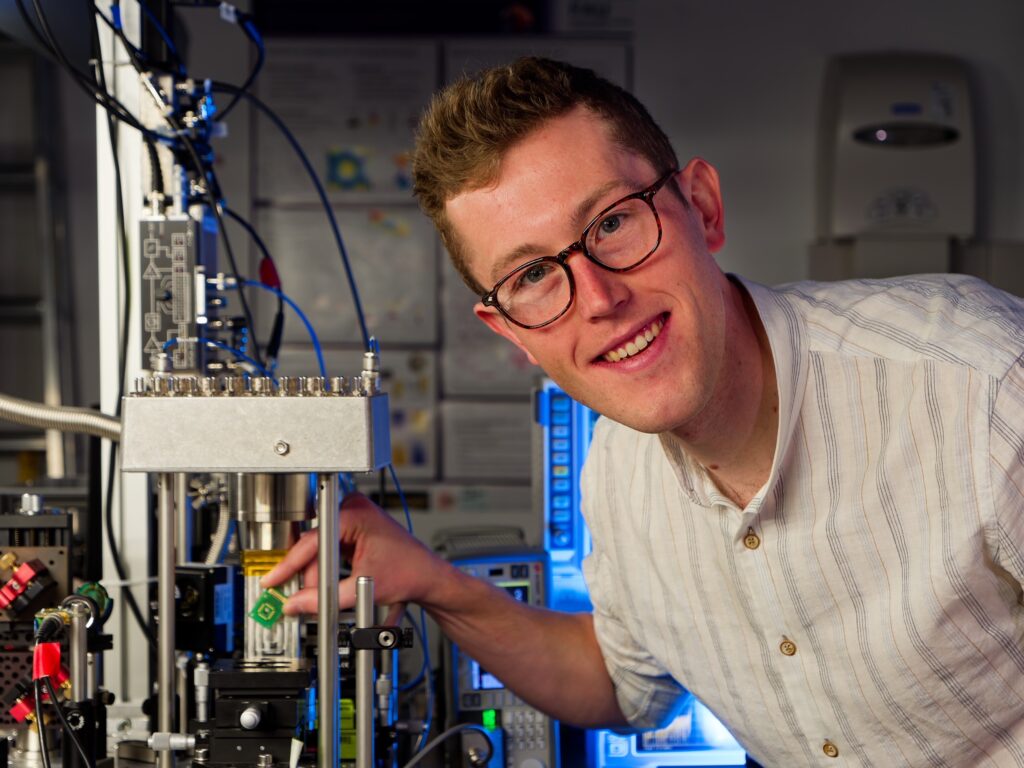 A young man wearing glasses at a physics experiment setup.